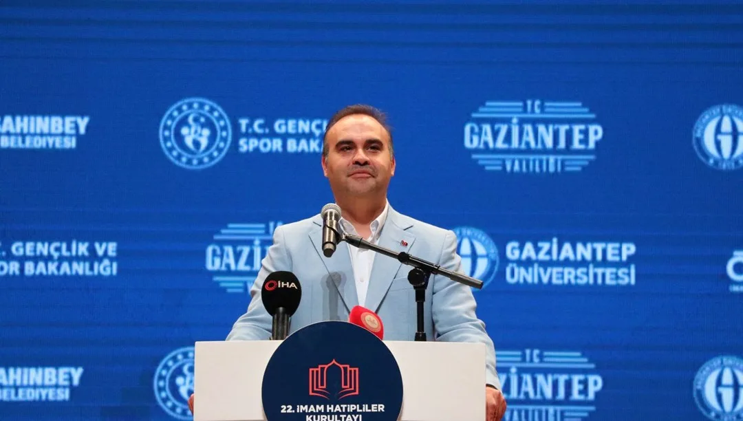 Bakan Kacır konuşurken mikrofonlar ve Türkiye bayrağı önünde kürsüde duruyor