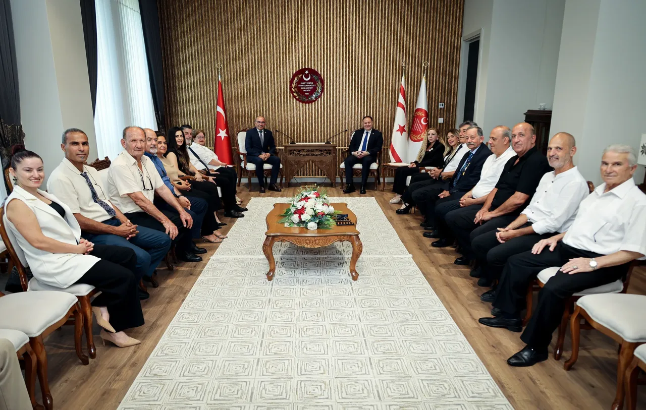 Öztürkler konuşurken mikrofon ve resmi arka plan önünde ifadeli poz