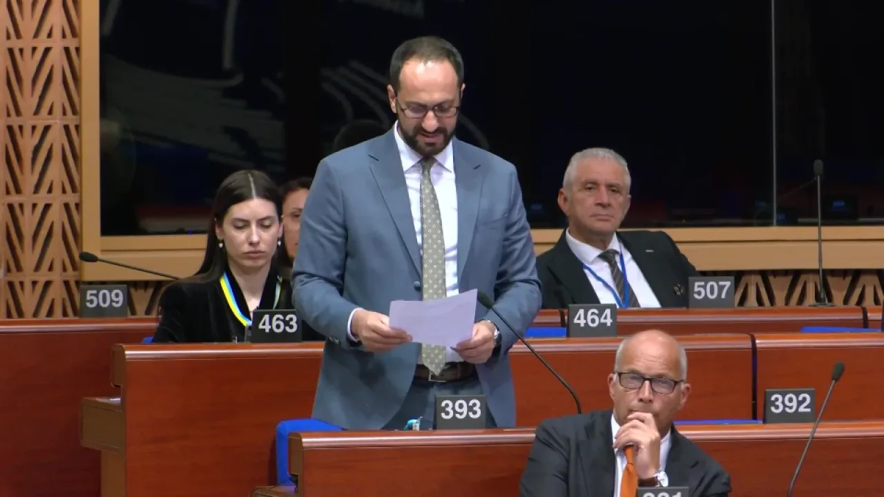 Armağan Candan konuşurken mikrofon ve masa üzerinde AKPA yazılı dökümanlar