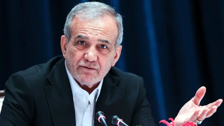 İran Cumhurbaşkanı konuşma yaparken elini kaldırmış, arka planda bayrak ve kürsü izleniyor