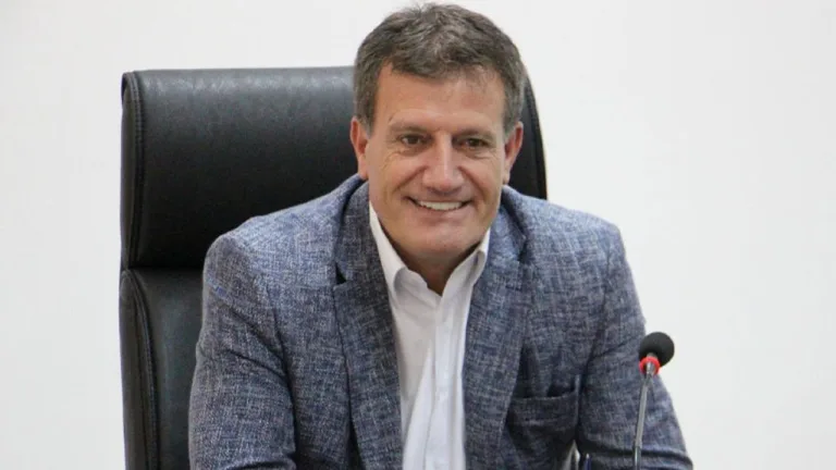 Erhan Arıklı konuşma yaparken mikrofon ve ceketli hali, arka plan flu