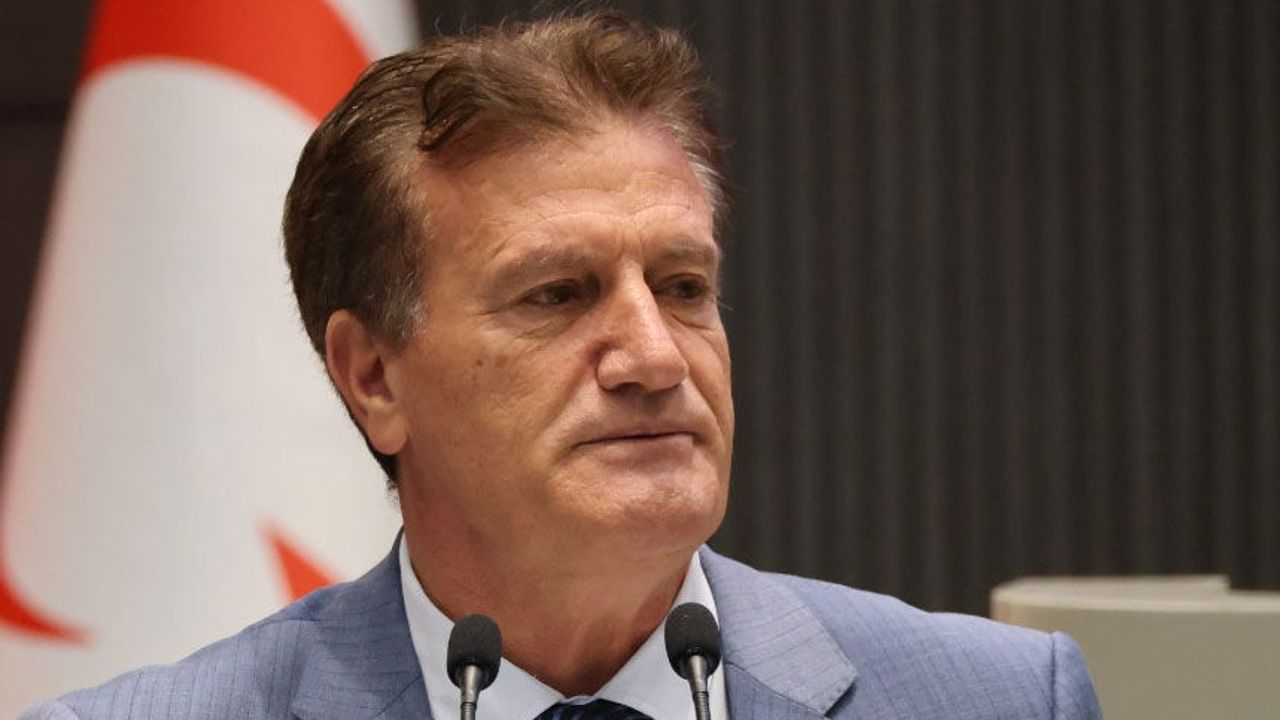 Arıklı konuşurken mikrofon ve ceketli görüntü; yüz ifadesi ciddi ve kararlı görünüyor