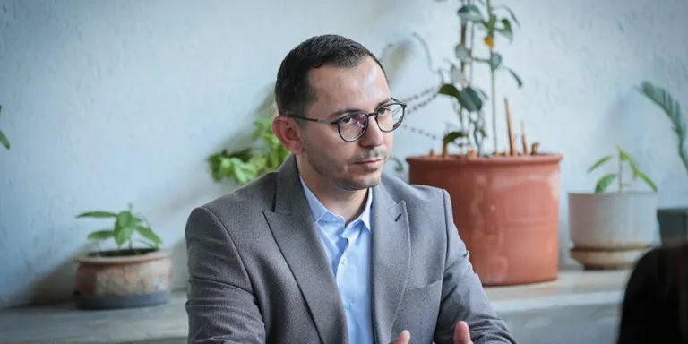 Üredi konuşurken mikrofon önünde ciddi ifadeyle oturuyor.