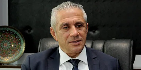 Hasan Taçoy mikrofonlar önünde konuşuyor, kararlı ifadeyle açıklama yapıyor