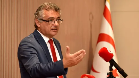 Erhürman konuşuyor; arka planda Kıbrıs'la ilgili görseller ve toplantı atmosferi