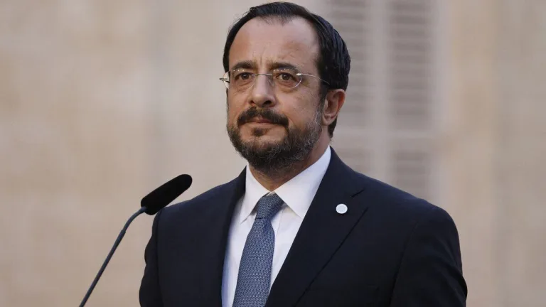 Nikos Hristodulidis konuşurken ciddi bir ifadeyle mikrofon önünde duruyor.