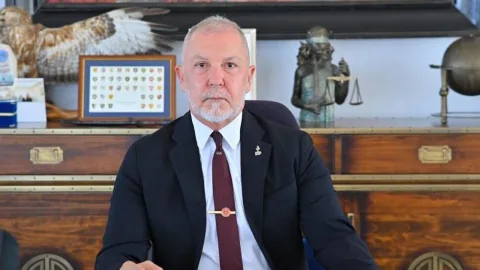 Akpınar konuşma yaparken mikrofonlara bakıyor; arka planda parti renkleri ve semboller belirsiz.