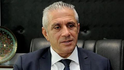 Taçoy konuşma yaparken mikrofon önünde ciddiyetle dinleyen kişilerle birlikte