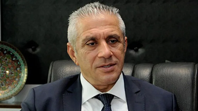 Taçoy konuşma yaparken mikrofon önünde ciddiyetle dinleyen kişilerle birlikte