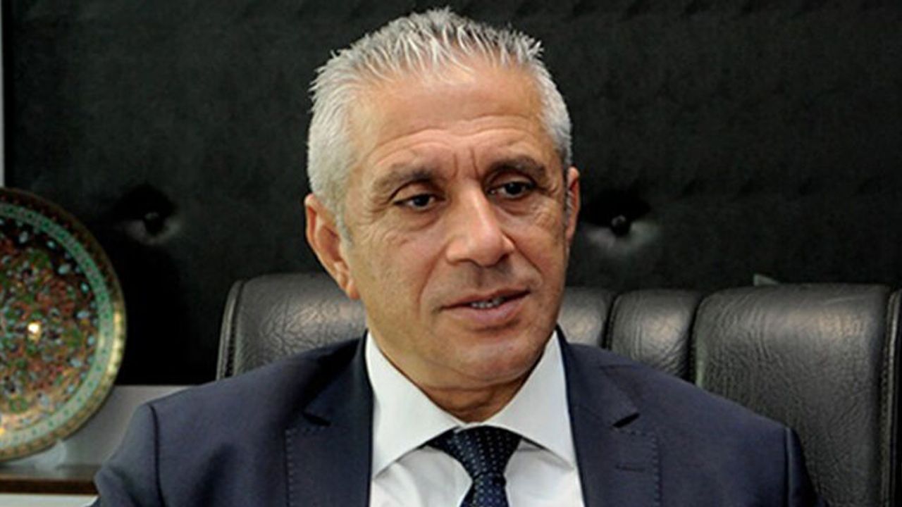 Taçoy konuşma yaparken mikrofon önünde ciddiyetle dinleyen kişilerle birlikte