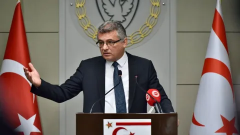 Erhürman konuşuyor; yüz ifadesi ciddi, arka planda konferans ortamı