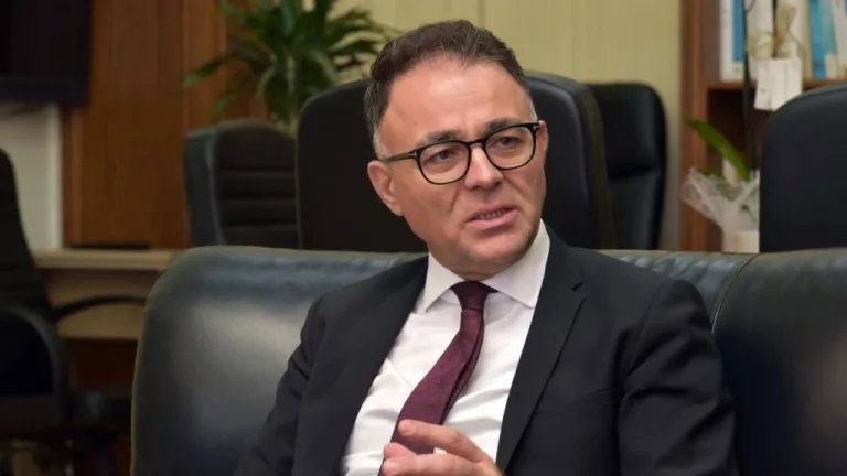 Sinirli ifadeli Özerdağ konuşurken, mikrofon ve arka planda parti logosu görünür