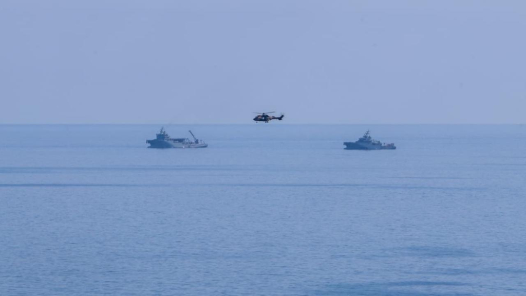 Üstel konuşurken, arka planda deniz ve kurtarma çalışmaları için bekleyen ekipler ve ekipmanlar