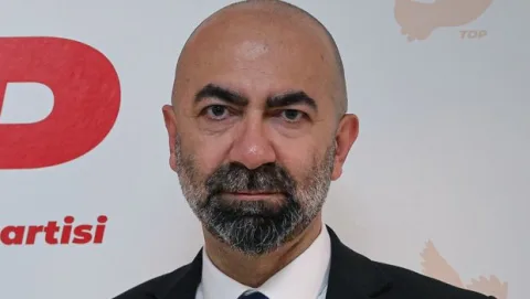 Kemal Baykallı konuşurken mikrofon önünde, arka planda TDP logosu ve parti renkleri
