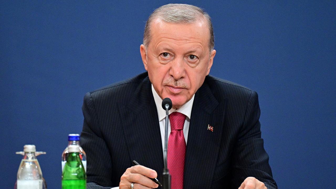 Cumhurbaşkanı Erdoğan konuşurken kürsüde duruyor, arka planda devlet sembolleri ve dinleyiciler görünüyor olabilir