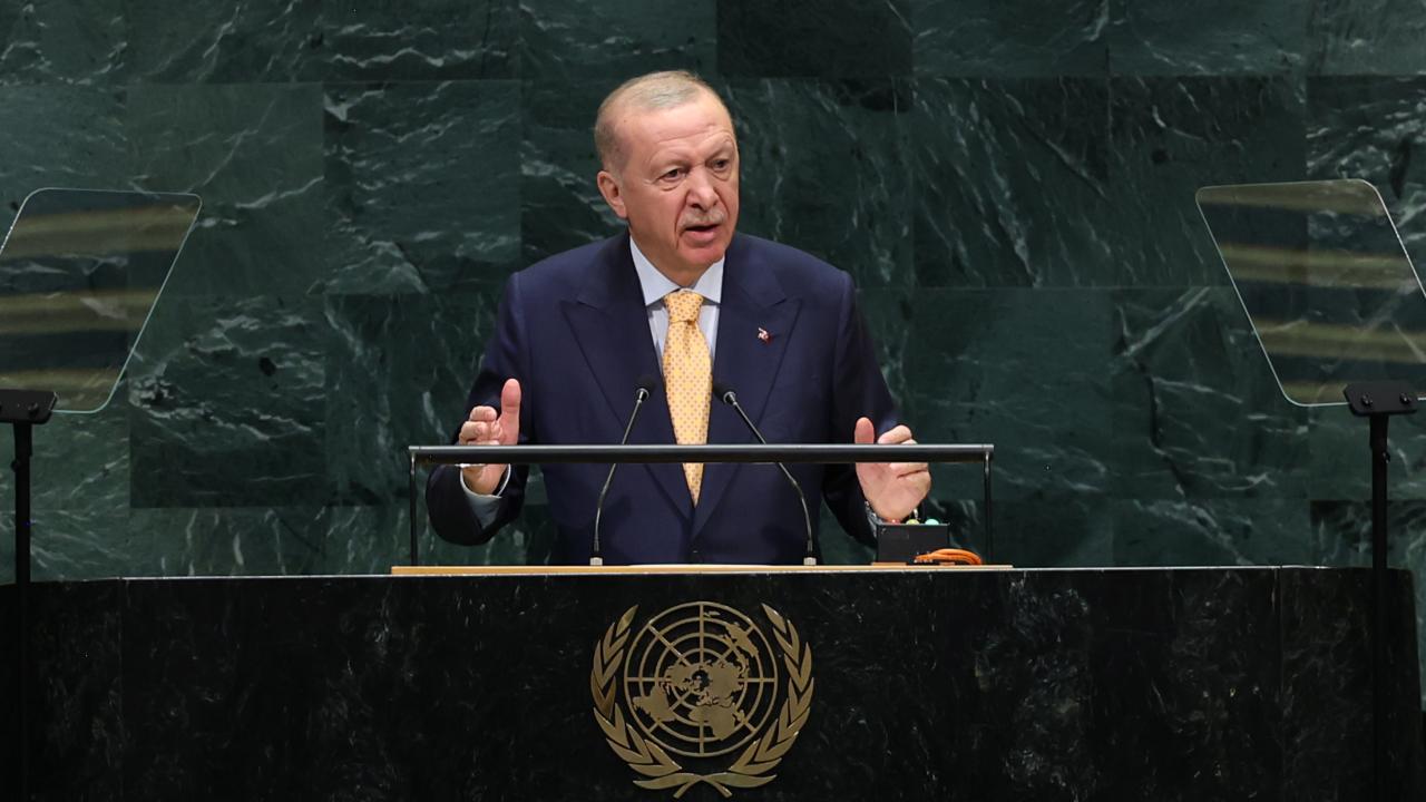 Cumhurbaşkanı Erdoğan konuşma yaparken kürsü önünde mikrofonlar ve Türk bayrağıyla görüntüleniyor