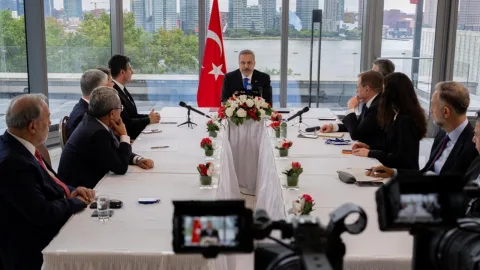 Bakan Fidan konuşma yaparken mikrofon önünde, ciddi ifade ve arka planda siyah fonlu görüntü