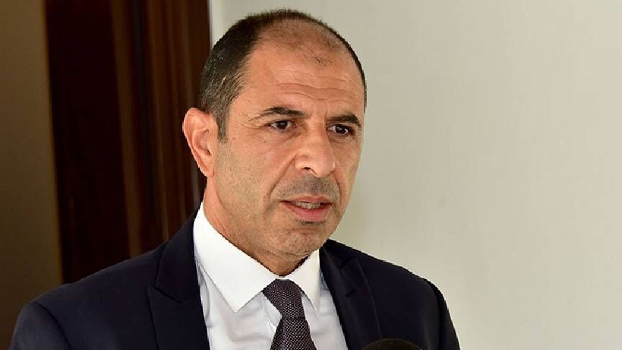 Özersay konuşurken kürsüde mikrofon ve arka planda toplantı ortamı