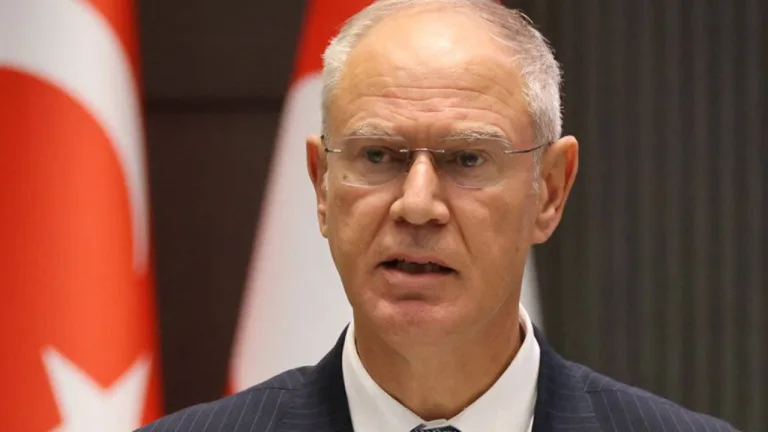 Hasipoğlu konuşurken mikrofon önünde duruyor; arka planda Maliye yazılı görsel veya pankart bulunuyor