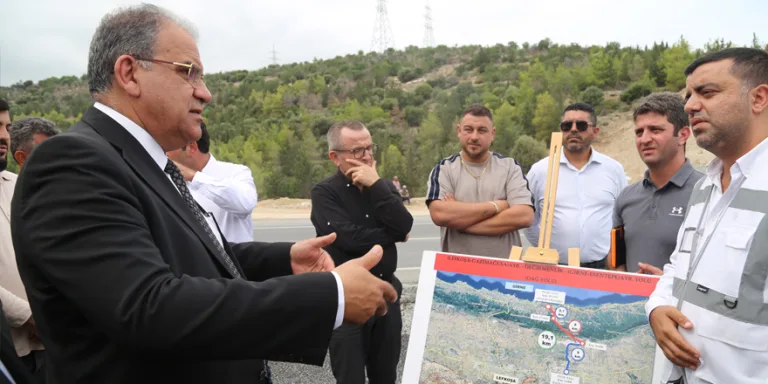 Sucuoğlu konuşurken, arka planda dağlık bölge fotoğrafı ve çalışma ekipleri görünüyor
