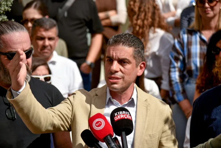 KTAMS Başkanı Yiğit konuşurken ciddi ifadeyle el hareketi yapıyor, arka planda parti ya da sendika simgeleri görünür.