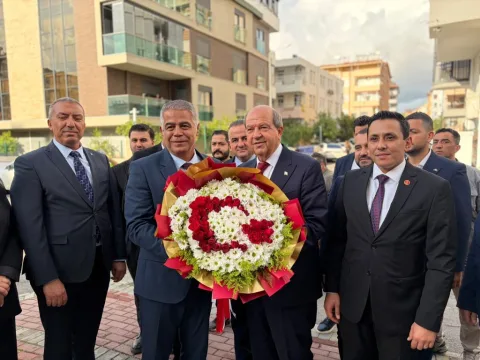 Tatar konuşma yaparken mikrofonlar ve Türkiye ile KKTC bayrakları arka planda