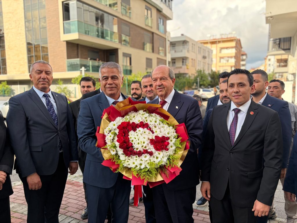 Tatar konuşma yaparken mikrofonlar ve Türkiye ile KKTC bayrakları arka planda