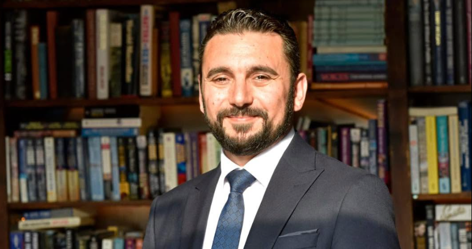 Tacan Reynar konuşurken kürsü ve mikrofonların önünde duruyor