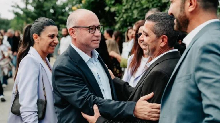 Reşat Kansoy konuşma yaparken, arkada Güzelyurt’a ait paneller ve yerel halk görünür.