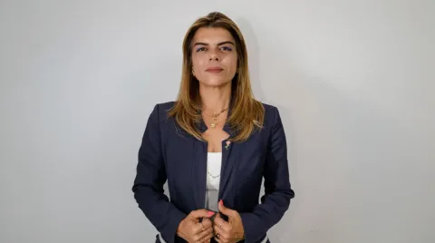 Ayşe Öztabay konuşma yaparken mikrofonlara bakıyor; arka planda siyasi pankartlar ve izleyiciler var