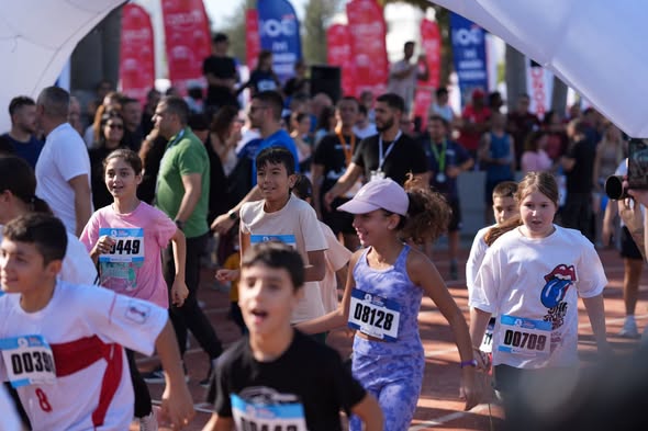 Koşucuların kalabalığı maraton pistinde ilerliyor, bariyerler ve izleyiciler kenarda yer alıyor