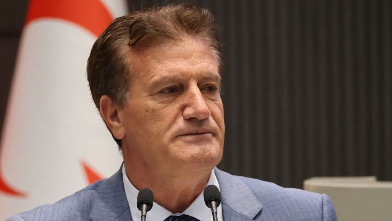 Erhan Arıklı konuşurken mikrofonlara bakıyor, arka planda boş beyaz zemin