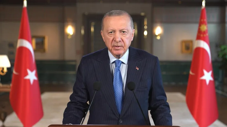 Cumhurbaşkanı Erdoğan kürsüde konuşuyor, arka planda Türkiye bayrağı ve toplantı atmosferi