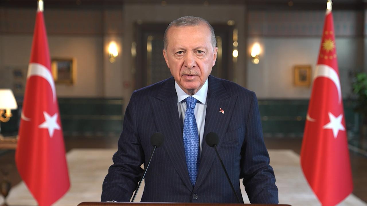 Cumhurbaşkanı Erdoğan kürsüde konuşuyor, arka planda Türkiye bayrağı ve toplantı atmosferi