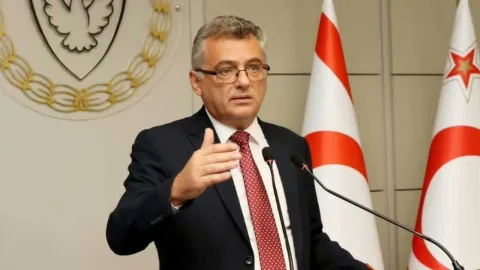 Erhürman konuşurken ciddi bir ifadeyle dinleyenler ve arka planda bayrak veya kürsü izlenimi