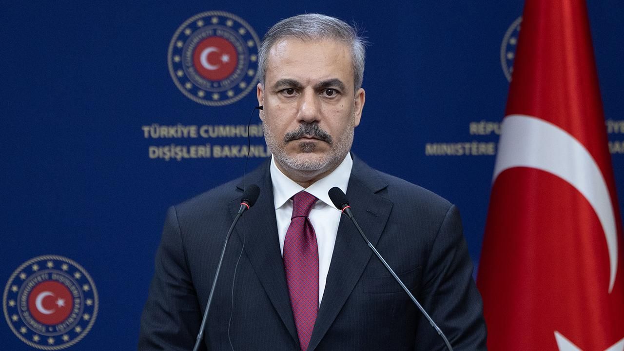 Fidan konuşurken ciddiyetle dinleyen kişilerle birlikte kürsü veya toplantı ortamı