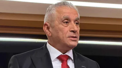 Taçoy konuşurken mikrofon ve akaryakıt istasyonuna ait pano görünüyor