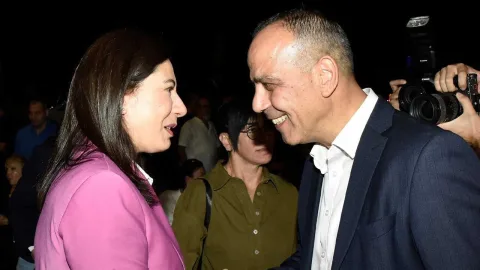 Harmancı konuşma yaparken mikrofonlara bakıyor, arka planda slogan ve partililer görünüyor
