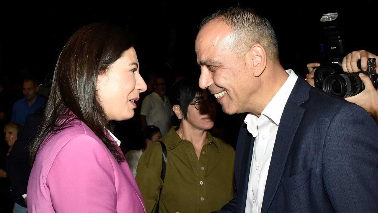 Harmancı konuşma yaparken mikrofonlara bakıyor, arka planda slogan ve partililer görünüyor