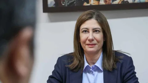 İncirli konuşma yaparken mikrofon ve kürsü önünde, arka planda toplantı salonu silueti