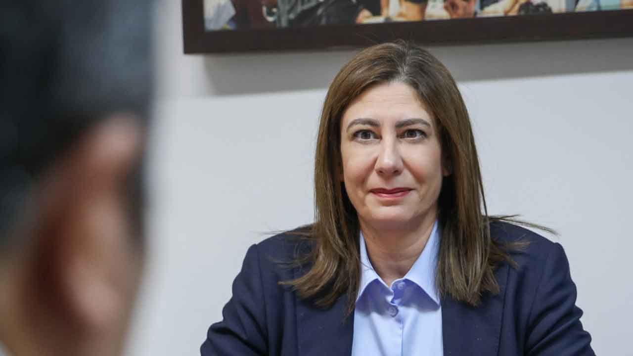 İncirli konuşma yaparken mikrofon ve kürsü önünde, arka planda toplantı salonu silueti
