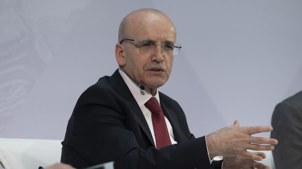 Bakan Şimşek konuşurken, arka planda sunum ve grafikler yer alıyor