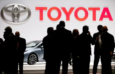 Toyota yetkilileri konuşurken, arka planda marka logosu ve otomobil silueti görülüyor