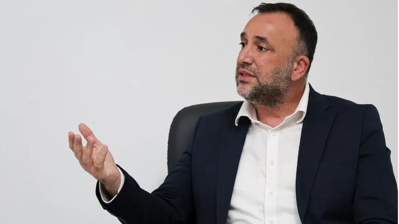 Zeki Çeler konuşma yaparken mikrofonla bakıyor, arka planda eğitim ve üretim vurgulu sloganlar