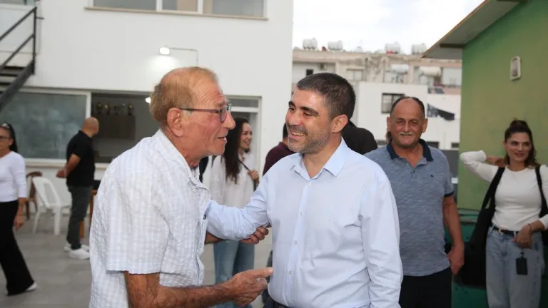 Aktunç konuşma yaparken kalabalığa bakıyor; arka planda belediye logosu ve bayraklar görünüyor