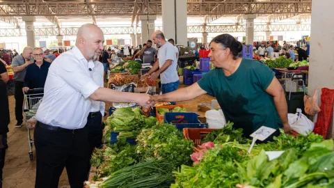 Bozkurt konuşurken mikrofonun önünde, toplantı veya ziyaret ortamında esnafla etkileşim görüntüsü