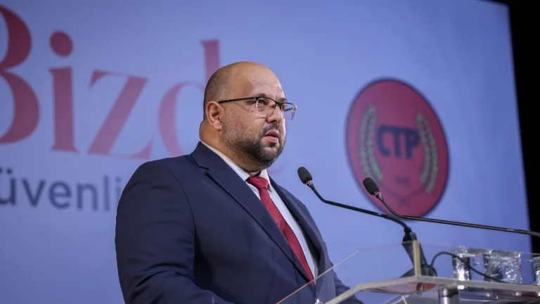 CTP Genel Sekreteri Kişi konuşurken mikrofon önünde, arka planda parti logosu ve destekleyenler
