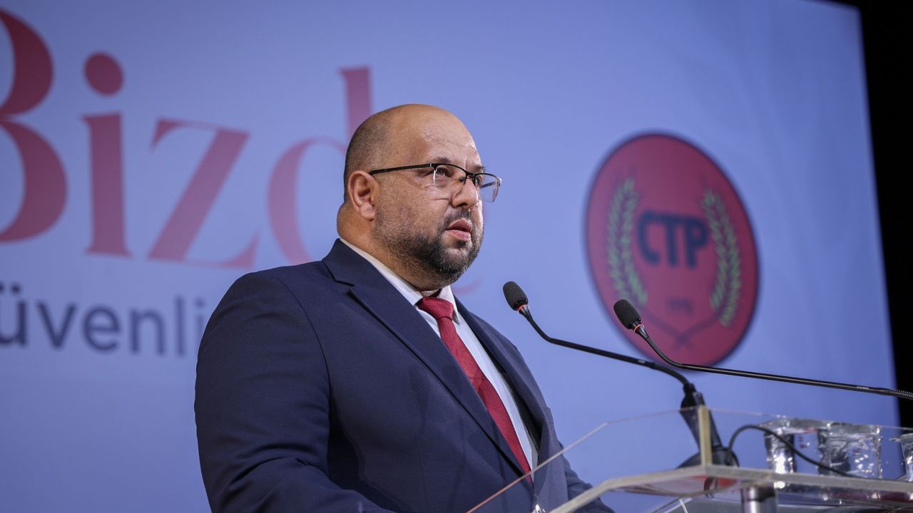 CTP Genel Sekreteri Kişi konuşurken mikrofon önünde, arka planda parti logosu ve destekleyenler