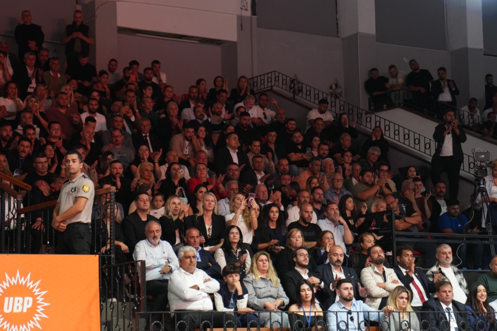 Üstel konuşma yaparken kalabalığa el sallıyor, arka planda parti bayrakları ve destekçiler görülüyor