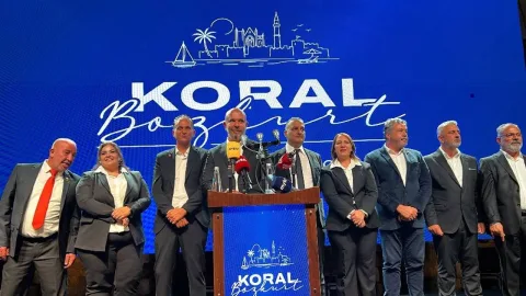 Bozkurt konuşurken mikrofon önünde duruyor, resmi etkinlik ortamı.